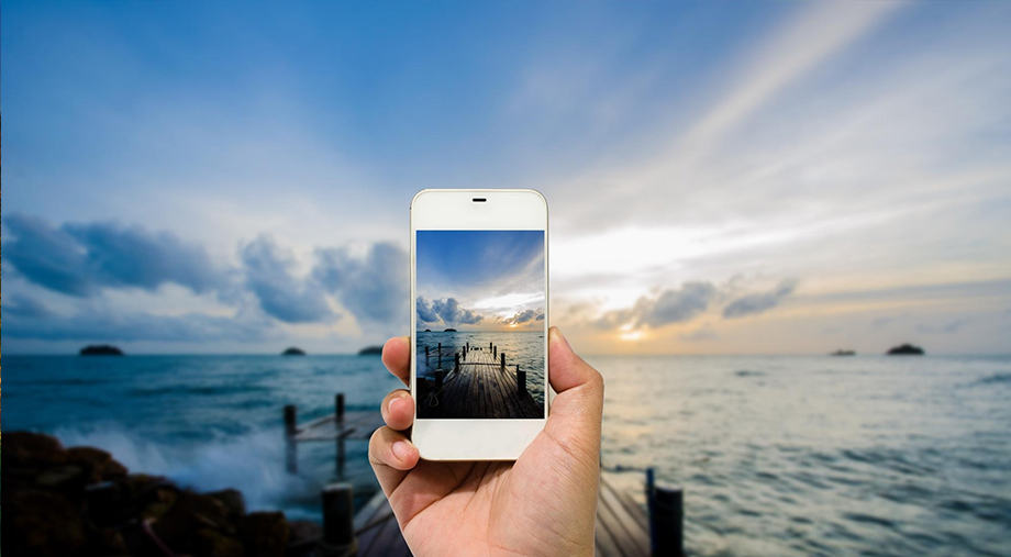Hand holding a phone in front of a sunset sea view